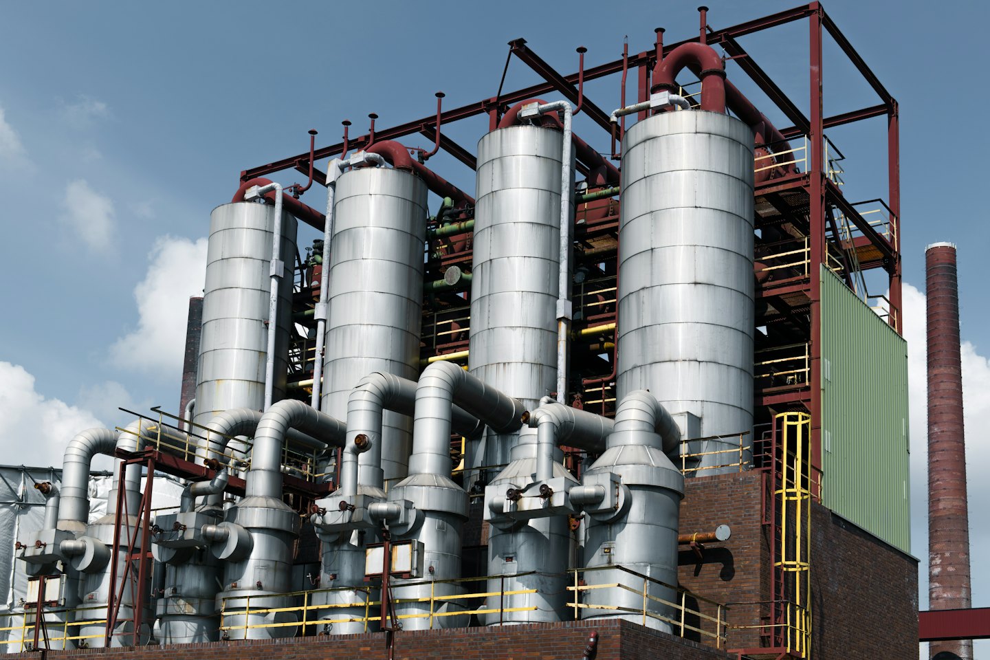 Industrial facility with large silver vessels and red piping.