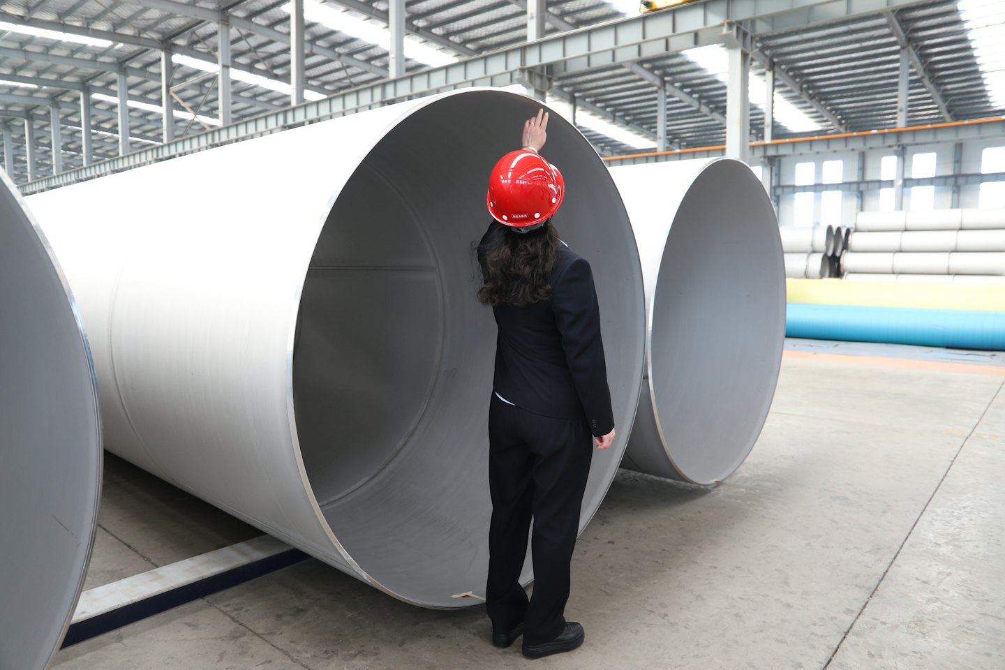 Engineer in a red hard hat points toward factory pipes.